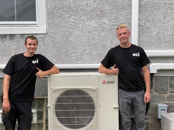 Two ECI Comfort employees standing side by side next to one of the outdoor units they installed in Huntingdon Valley home. 