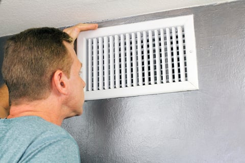 man looking at white heater vent
