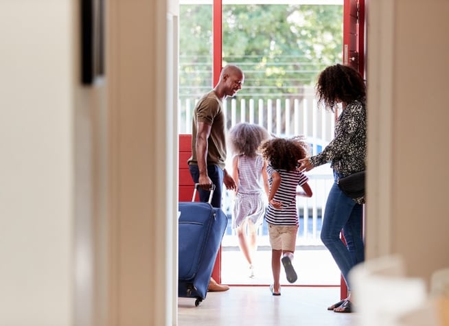 family-standing-by-front-door-with-suitcase-about-to-leave